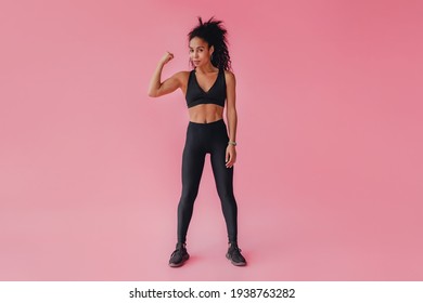 Attractive Black African American Woman In Black Leggings And Top Fitness Outfit On Pink Isolated Background, Confident Curly Hair Sport Style, Athletic Body, Strong Muscles