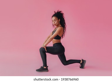 attractive black african american woman in black leggings and top fitness outfit on pink isolated background, confident curly hair sport style, athletic body, work out