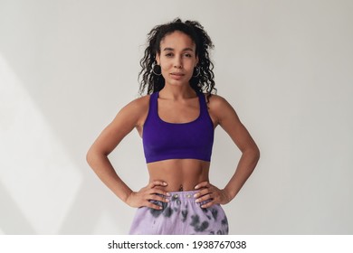 attractive black african american woman in stylish hipster fitness outfit violet top and pants on white isolated background, summer fashion trend, happy smiling curly hair sport style