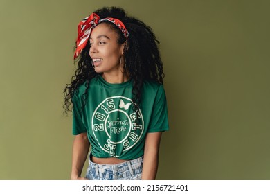 Attractive Black African American Woman In Stylish Hipster Outfit T-shirt And Shorts On Green Studio Background, Summer Fashion Trend, Happy Smiling Curly Hair Red Headband And Earrings Accessories