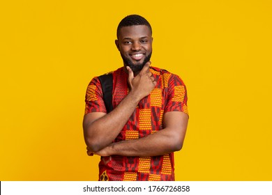 Attractive black man in authentic clothes touching his chin and smiling, yellow background