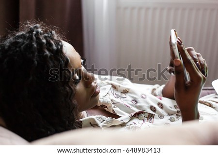 Attractive black woman lying on the sofa with the phone in her hands. Woman has long dark curly hair.