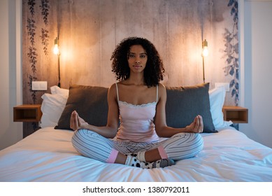 Attractive black woman sitting in lotus position on bed meditating - Powered by Shutterstock