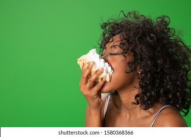 Attractive black woman taking messy bite of cake on greenscreen. Young woman making a mess eating dessert - Powered by Shutterstock