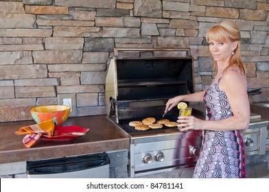 Attractive Blond Caucasian Woman Using A Gas Barbeque Grill In An Outdoor Kitchen