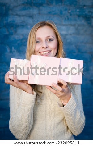 attractive blond young woman in woolen sweater receiving presents having fun happy smiling on blue brick wall background