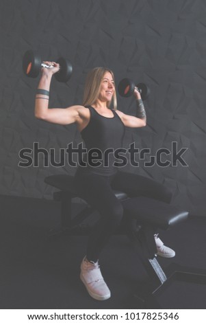 Attractive blonde athlete doing exercises with weights in the gym pumping up his arm muscles on dark background