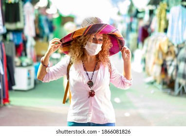 Attractive Blonde Curly Mature Woman At Flea Market Wearing A Large Multi Colored Hat Handicrafted -  Wearing Surgical Mask Due To Coronavirus Infection