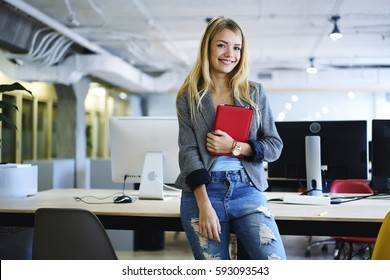 Attractive blonde female office manager supervising working process in office coordinating staff and preparing reporting on conference standing in modern studio with wireless connection and computers