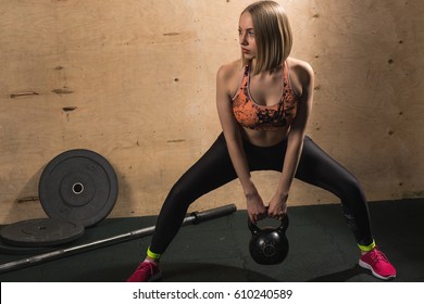 Attractive blonde girl doing exercises with kettle bell. Weightlifting, cross fit and power lifting workout. Sports, fitness concept.
