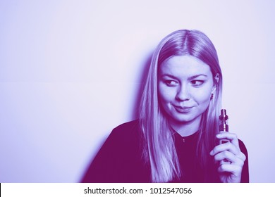 attractive blonde girl with an expressive look holding a vape device in her hands. Trendy duotone effect 