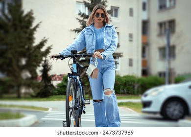 Attractive blonde in jeans pushing electric bicycle posing for the shot  - Powered by Shutterstock