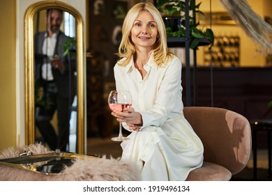 Attractive Blonde Lady Sitting Down And Smiling While Mirror Reflecting A Man Behind Her