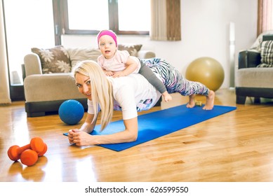 Attractive blonde mother in 30s doing fitness exercise in home with her baby daughter. Toned image. Authentic people.
