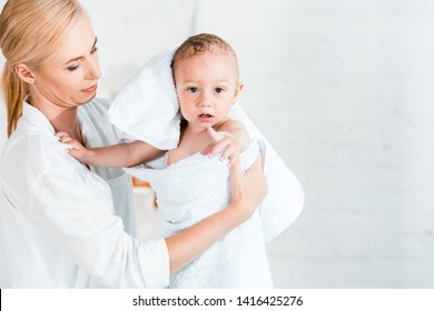 attractive blonde mother holding in arms adorable toddler son in bathroom 