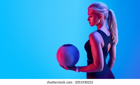 Attractive blonde sportswoman portrait holding with medicine fitness ball neon style creative light. Confident fitness woman standing with a medicine ball - Powered by Shutterstock