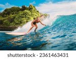 Attractive blonde surf girl riding on surfboard in ocean. Surfer on blue wave during surfing