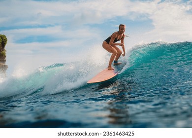 Attractive blonde surf girl riding on surfboard in ocean during surfing. Surfer on blue wave - Powered by Shutterstock