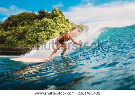 Attractive blonde surf girl riding on surfboard in ocean. Surfer on blue wave during surfing