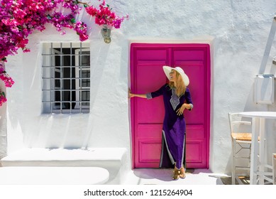 Attractive, blonde traveler woman in front of a traditional cylcadic house on the island of Paros, Naoussa, Greece