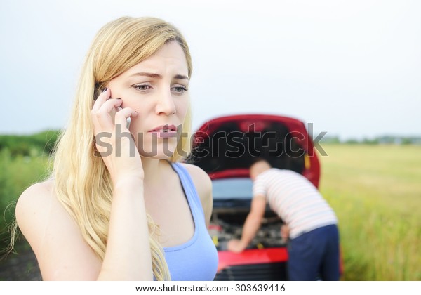 Attractive blonde woman call for help on the phone.
Damage to auto. Young couple cannot continue the way because of the
broken car.