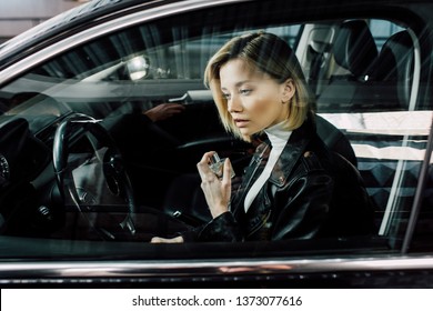 attractive blonde woman holding perfume bottle in car 