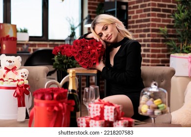 Attractive Blonde Woman Posing With Valentines Day Red Roses, Luxury Presents, Romantic Date. Young Girl With Expensive Flower Bouquet, Giftboxes, Macarons Sitting In Living Room