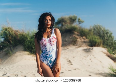 An attractive bright young girl in a swimsuit strolls along the sandy beach, looks thoughtfully aside, catches her looks, the wind disheveled her hair. The concept of rest, the journey, the island
