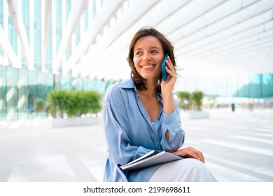 Attractive brunette businesswoman talking mobile phone with client. Pretty caucasian female business person smile when phone conversation. Woman managing business talking via mobile phone sitting - Powered by Shutterstock