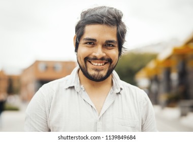 Attractive Brunette Latin Man Looking At The Camera And Smiling. Man Is On Foreground And Focus, Background Is Blurred.