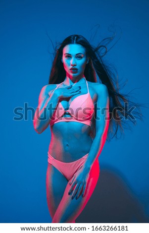 Attractive brunette model on blue studio background in neon light. Beautiful women in underwear posing with flying hair and dark make up. Concept of sensuality, style, fashion industry, characters.