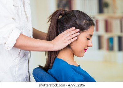Attractive brunette office woman wearing blue sweater sitting by desk receiving head massage, stress relief concept