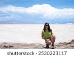 Attractive brunette and tanned latina woman posing crouching with the spectacular salinas grandes of argentina in the background with sunglasses on vacation on a blue sky day