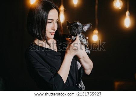attractive brunette woman with French Bulldog puppy in dark loft-style apartment with glowing lights hanging from ceiling. love of owners and pets. veterinary clinic. interior designer