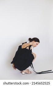 Attractive Brunette Woman Wear Navy Blue Cocktail Dress With Belt, Puff Sleeves, Open Naked Shoulders Pearls Earrings, Necklace Isolated On White Background. Full Length Woman With Low Bun Sitting.