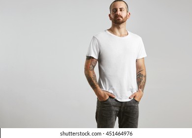 Attractive brutal tattooed bearded guy poses in black jeans and blank white t-shirt from premium thin summer cotton, isolated on white mockup