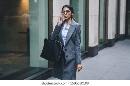Attractive business lady in elegant outfit and eyeglasses holding leather bag having phone call while talking at street of New York city - Shutterstock ID 1505030198