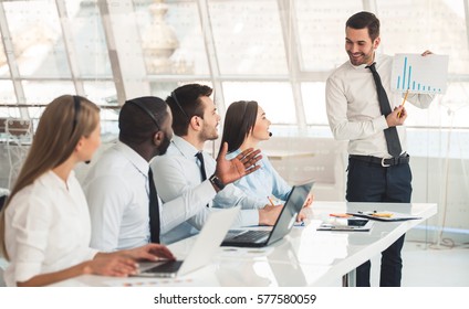 Attraktive Geschäftsleute in Anzügen und Headsets lächeln und hören ihrem Kollegen bei der Arbeit mit Laptops im Büro zu
