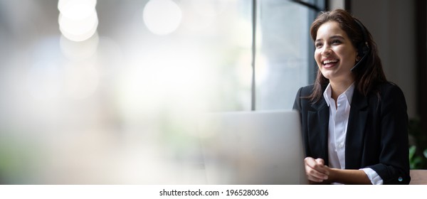 Atractiva mujer de negocios asiática con traje y auriculares sonriente mientras trabaja con computadora en la oficina. Asistente de servicio al cliente que trabaja en la oficina. Auriculares con micrófono de VOIP Helpdesk. fondo de banner panorámico