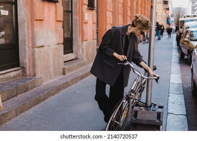 Attractive Business Woman Come To Sits On Bike. Girl Wear Grey Jacket Or Blazer, Black Pants, Eyeglasses. Modern Business Woman Ride To Work On Vehicle. Way To Office. Riding Bicycle To Work.