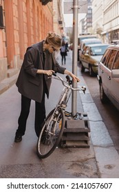 Attractive Business Woman Come To Sits On Bike. Girl Wear Grey Jacket Or Blazer, Black Pants, Eyeglasses. Modern Business Woman Ride To Work On Vehicle. Riding Bicycle To Work. Focus On Bike.