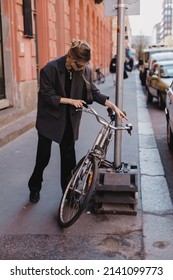 Attractive Business Woman Come To Sits On Bike. Girl Wear Grey Jacket Or Blazer, Black Pants, Eyeglasses. Modern Business Woman Ride To Work On Vehicle. Riding Bicycle To Work. Focus On Bike.