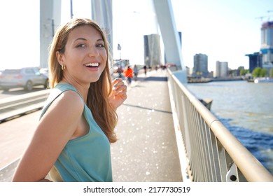 Attractive business woman on bridge turns around and smile to the camera with Rotterdam cityscape on the background, Netherlands