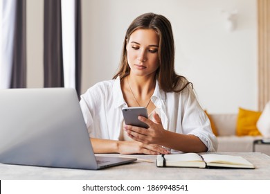 Attraktive Geschäftsfrau sitzt am Tisch vor dem Laptop und verwendet Smartphone für die Arbeit.