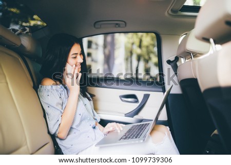 Attractive business woman working on her laptop at the back sit of a car and talking on the phone on the way to meeting