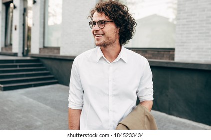 Attractive businessman in eyewear smiling broadly posing outdoors. Male entrepreneur resting in the city street. The curly guy in casual wears spectacles with curly hair walking outside after work