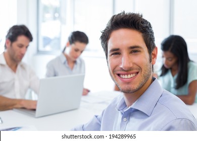 Attractive businessman smiling at the camera whilst working with coworkers