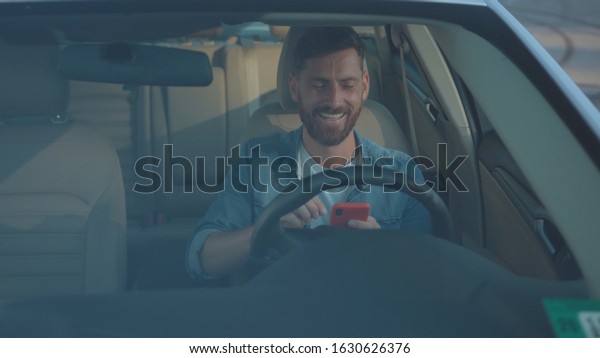 Attractive businessman\
texting in social network on smartphone sitting in modern car.\
Profile of handsome sociable guy with mobile phone planning a route\
through city.