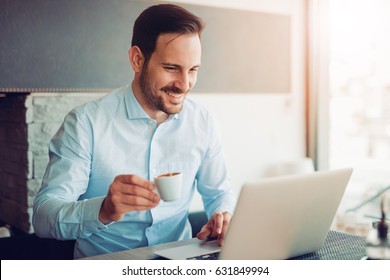 Attractive Businessman Using A Laptop And Smiling While Working In Cafe.