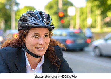 Attractive Businesswoman Commuting On A Bicycle Cycling To Work Along A Busy Urban Street, Close Up Head And Shoulders In A Safety Helmet